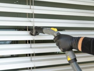 Person dusting fabric blinds with a soft brush.